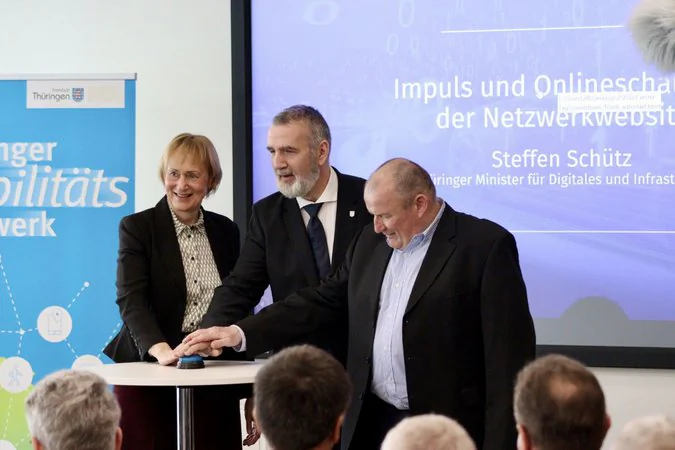 Frau Wosche (Geschäftsführung LEG), Herr Schütz (Minister des TMDI) und eine weitere männliche Person drücken vor Publikum auf einen Knopf