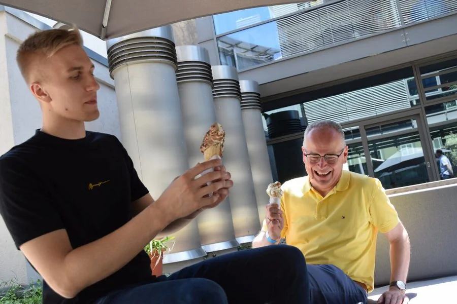 Zwei Männer sitzen auf einer Terrasse und genießen Eiscreme an einem sonnigen Tag.