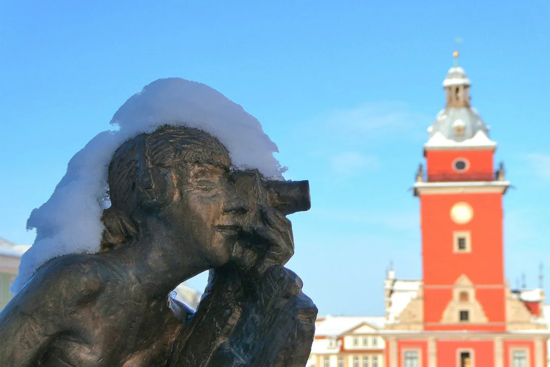 Eine Person mit Kamera als Statue, im Vordergrund eines roten Gebäudes.