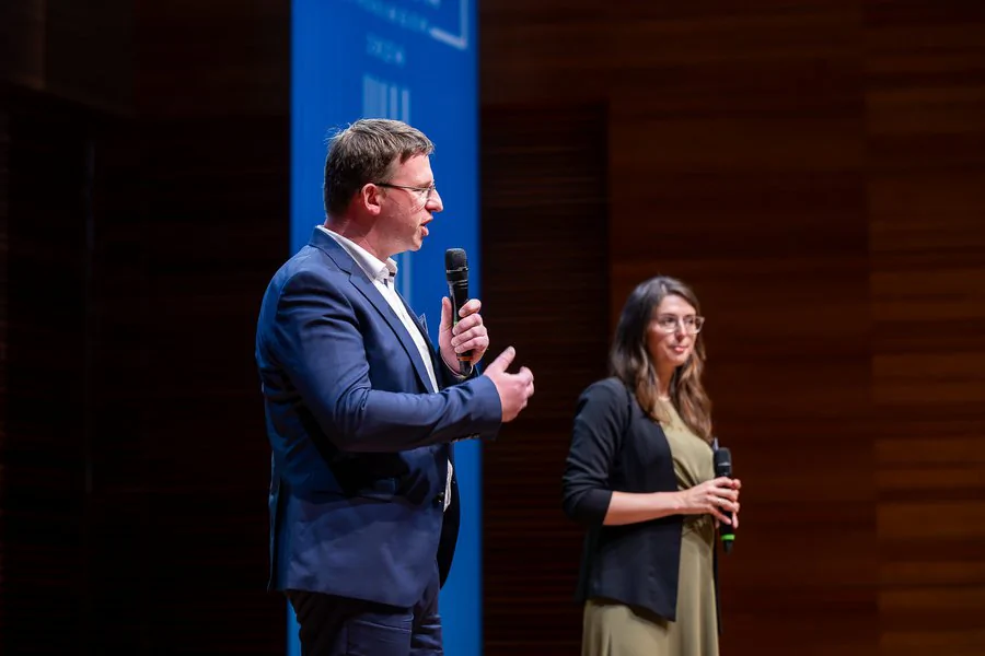Foto: Robert Weigelt (LEG) und ein weiterer Gast halten eine Rede auf der Bühne