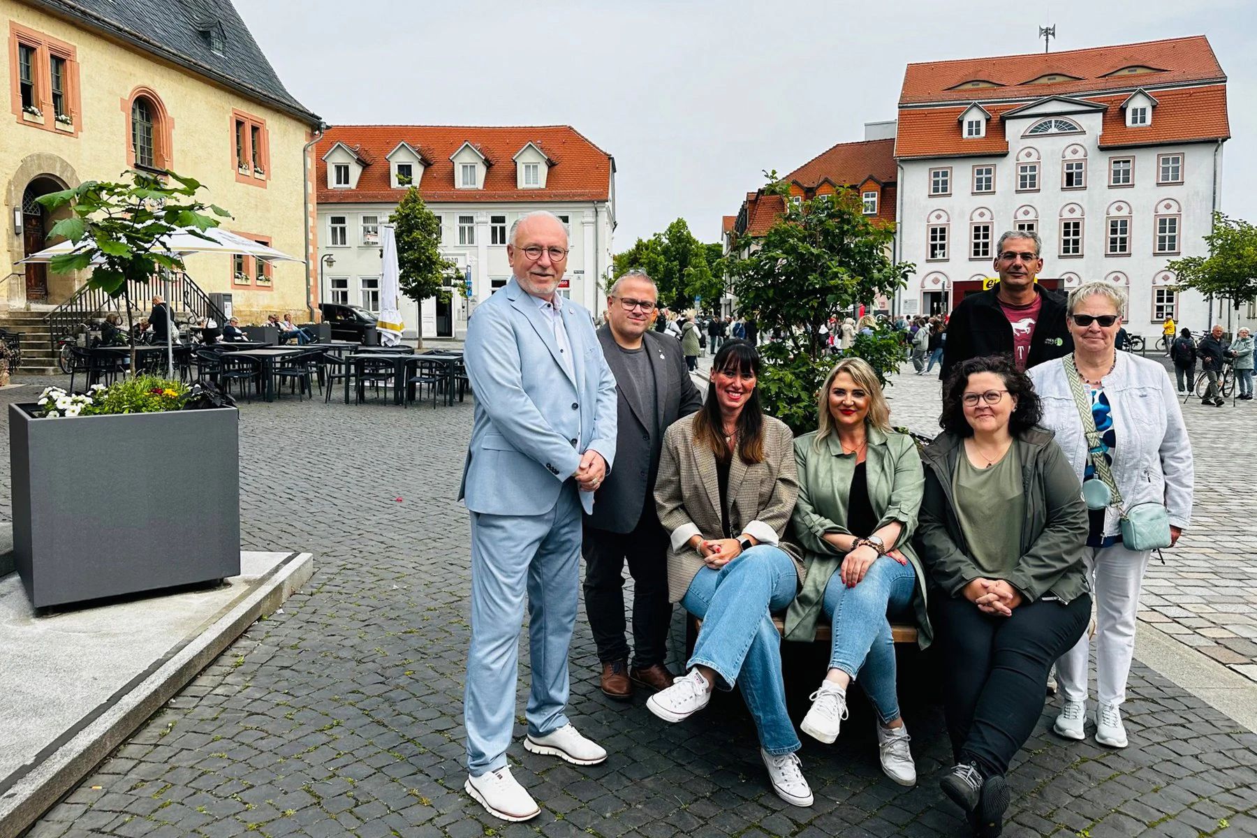 Projektbeteiligte sitzen auf einer Sitzbank in der Innenstadt Sömmerdas, umgeben von der Wanderbaumallee.