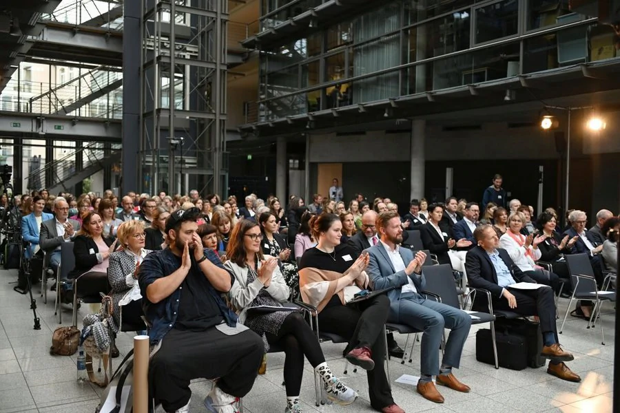 Eine große Menschenmenge sitzt in Stühlen im Atrium des COMCENTER und verfolgt eine Veranstaltung.