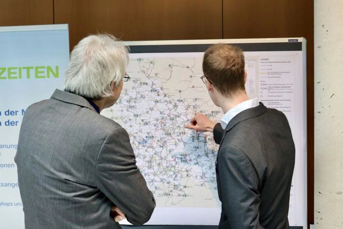 Zwei männliche Personen diskutieren an einer Pinnwand den integralen Taktfahrplan