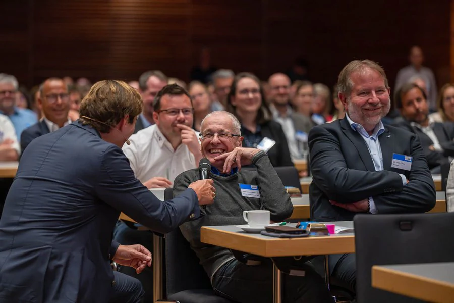 Der Keynote Sprecher unterhält sich mit einer lachenden Person im Publikum