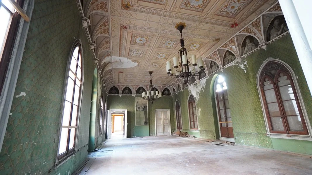 Das Innere eines verlassenen Schlosses mit grünen Wänden und aufwändiger Stuckdecken und zwei Kerzenkronleuchtern