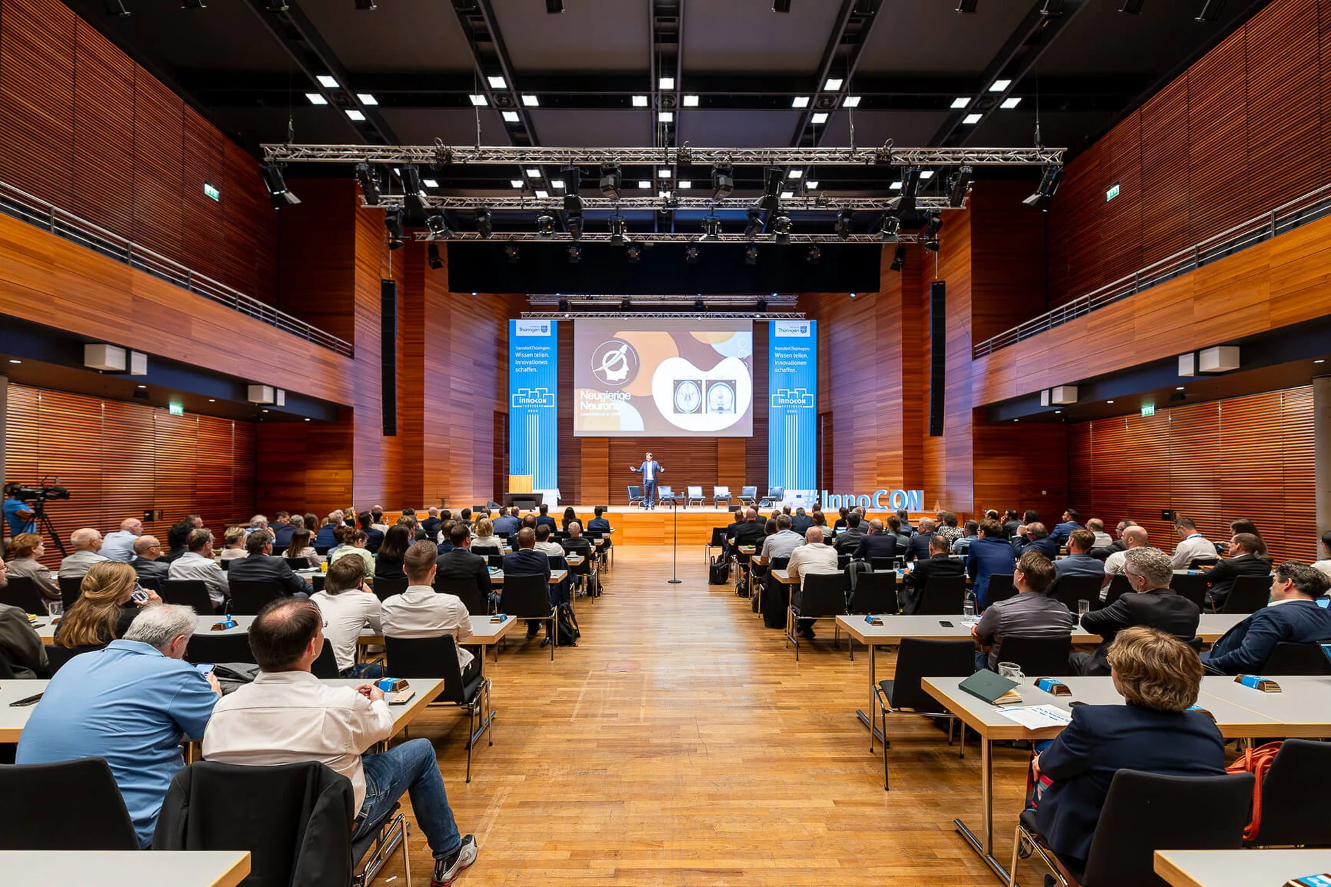 Menschen sitzen an Tischen in einem großen Auditorium