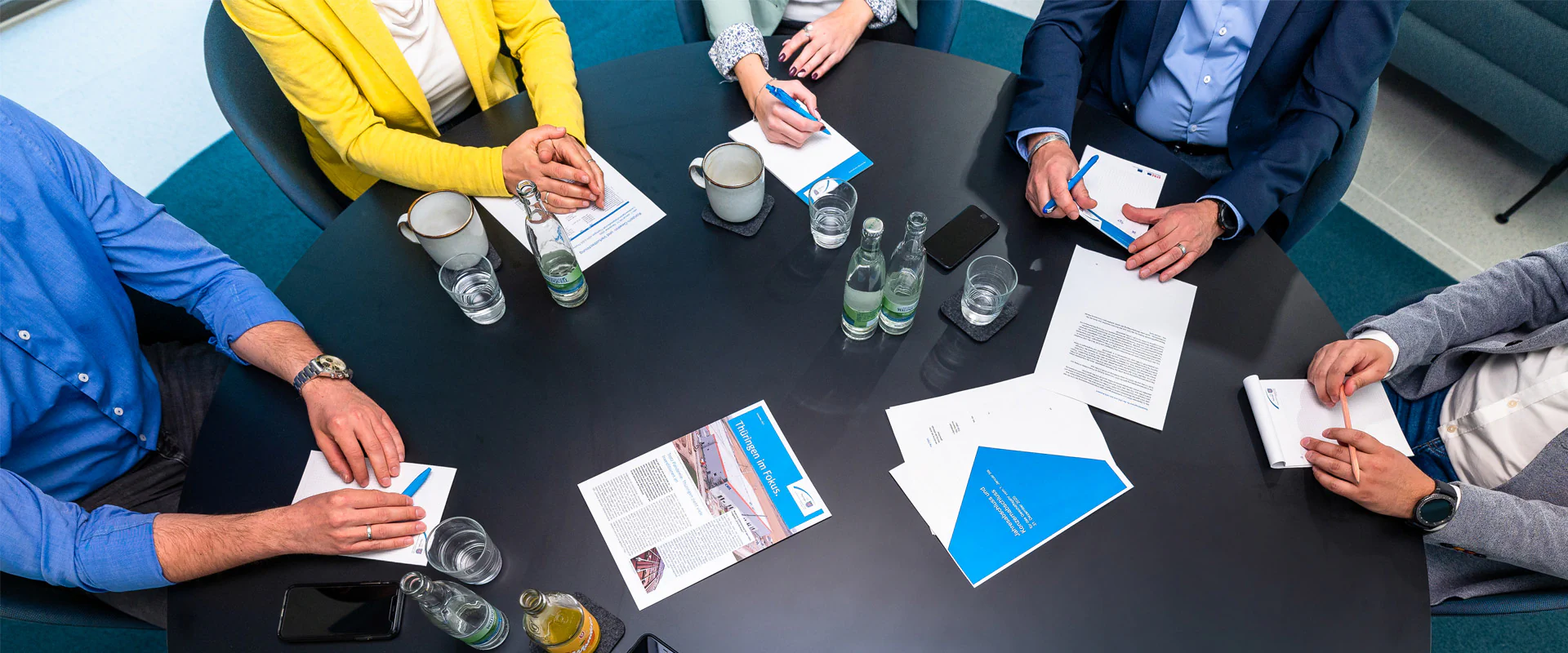 Bildbeschreibung / description: Eine Gruppe von Personen sitzt um einen Tisch und betrachtet gemeinsam Dokumente und Unterlagen.