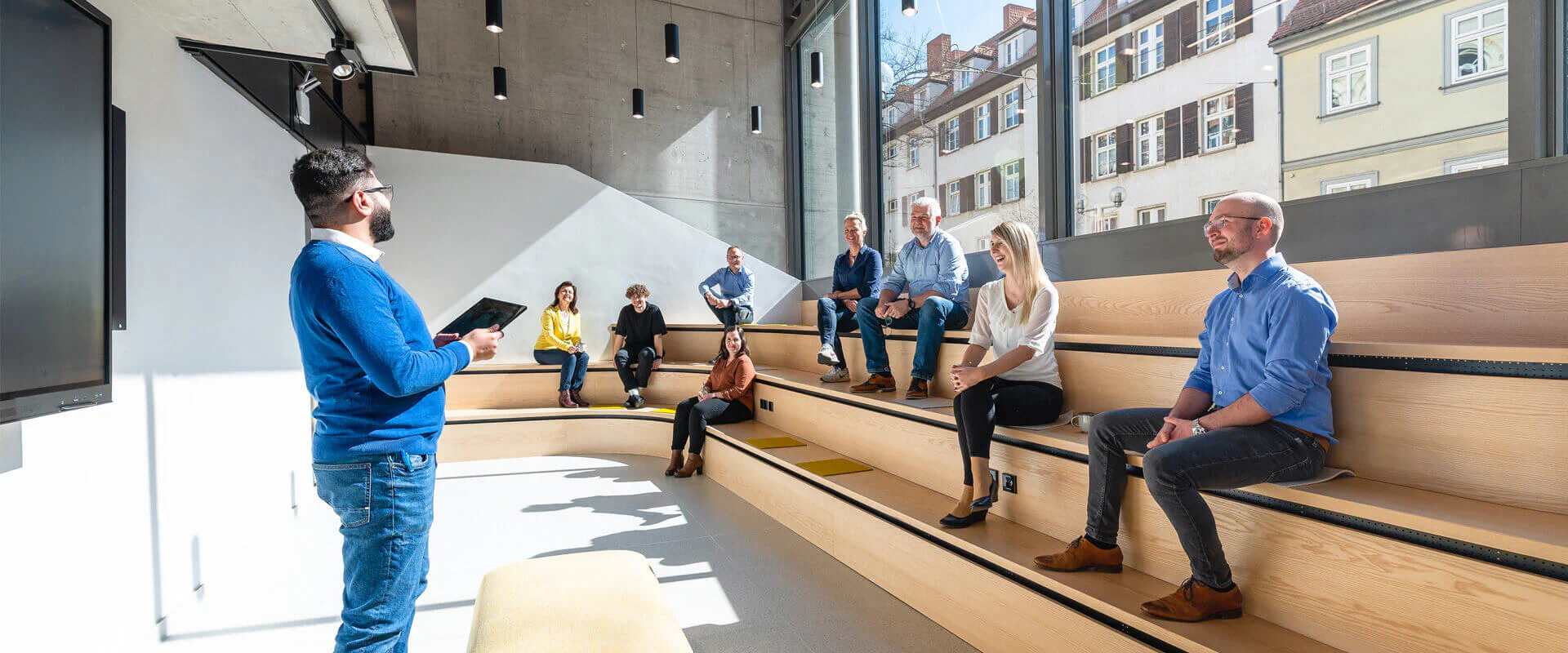 Bildbeschreibung / description: Eine Gruppe von Personen lauscht einer Präsentation in einer Art Amphitheater