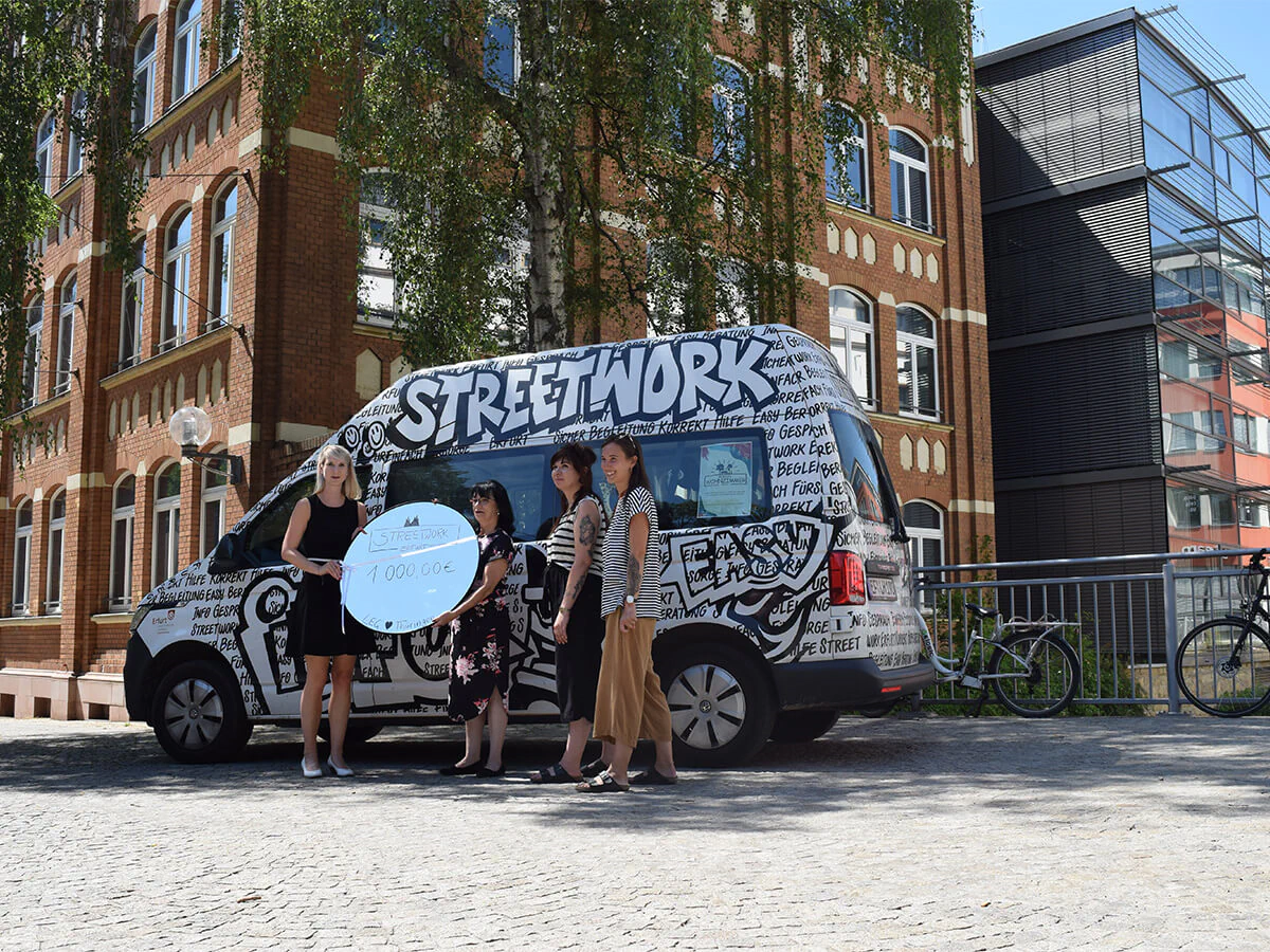 Bildbeschreibung / description: Übergabe vor einem schwarz-weiß beklebtem Kleinbus beim LEG Gebäude