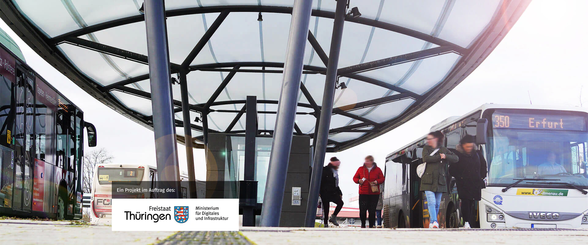Bildbeschreibung / description: Menschen steigen an einer Bushaltestelle ein und aus einem Bus, während andere auf der Straße warten, Logo des Wirtschaftsministeriums Thüringen unten Links
