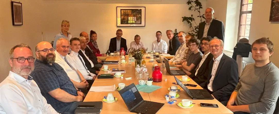 Bildbeschreibung / description: Projektbeteiligte sitzen gemeinsam an einer Tafel und schauen in die Kamera